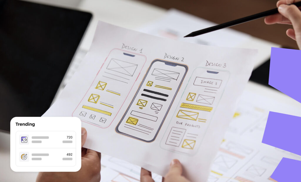 A close-up of hands holding a paper showing three mobile app screen wireframe sketches to compare layout options